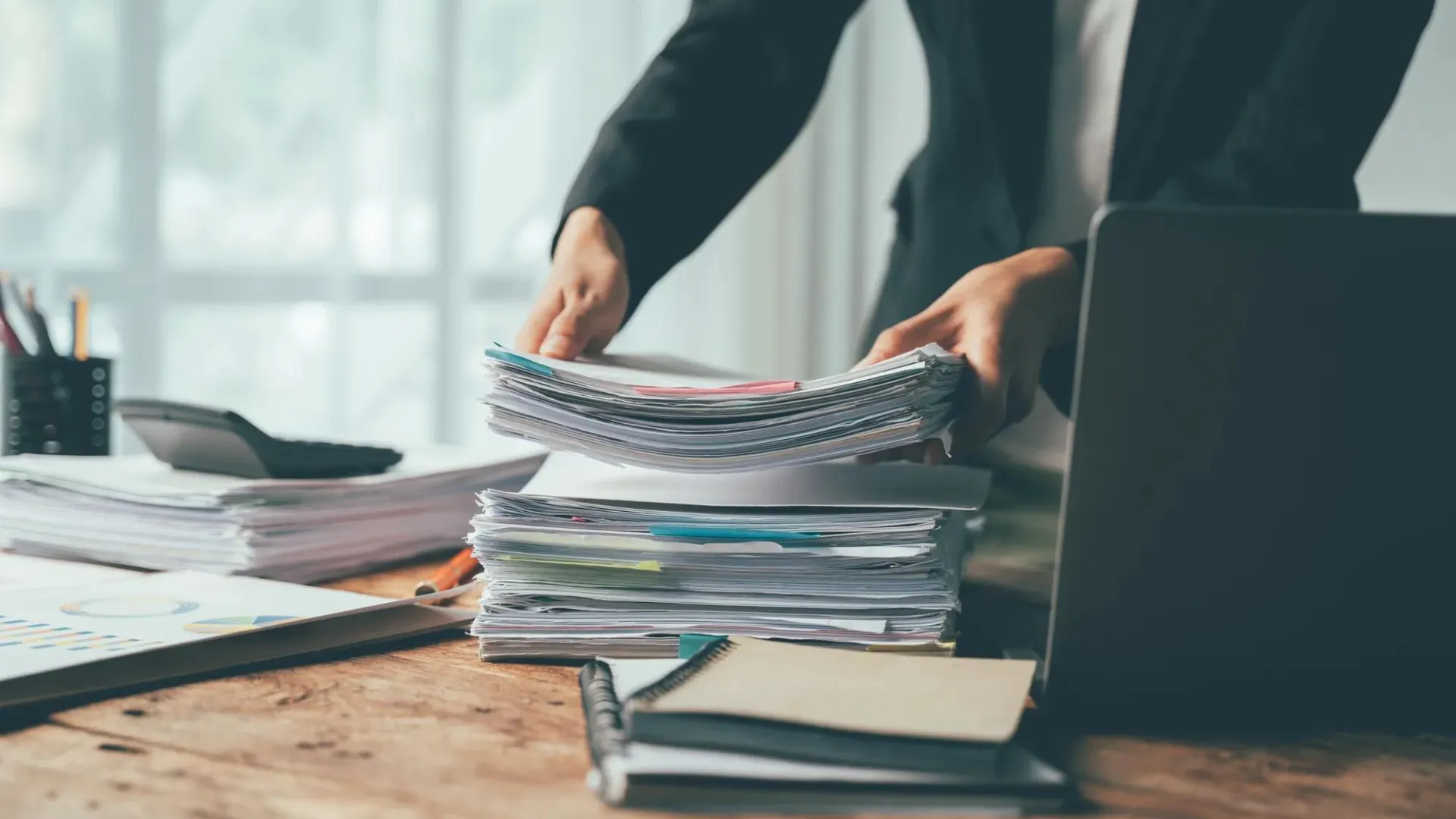 A person putting a stack of papers on a desk