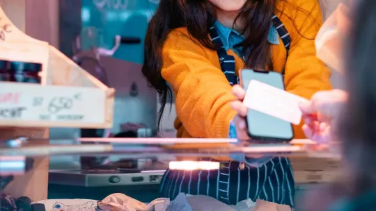 A young woman behind the counter at a butcher shop receives a digital payment from a customer. 